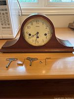 Antique Ergo mantel clock on wooden surface with four winding keys and small metal parts in front