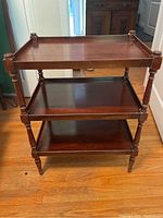 Front view of antique three-tier wooden shelf showing turned legs and raised edges on top shelf