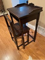 Angle view of antique telephone table with chair, showing wood finish, table top, and chair backrest detail.