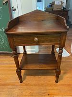 Full view of antique wooden washstand showing turned legs, raised backboard with side wings, single drawer, and lower shelf.