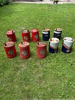 Ten oil cans arranged on grass—mix of red B/A and white/navy Gulf cans