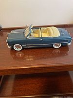 Side view of blue 1949 Ford Maisto model car showing convertible cream-colored interior on wooden surface.