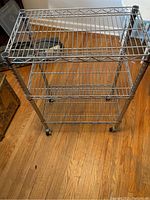 Top-down view of metal rolling shelf unit showing three wire shelves and caster wheels.