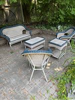 Full set of resin wicker patio furniture including loveseat, 2 chairs, coffee table, side table, placed outdoors on stone patio with surrounding greenery