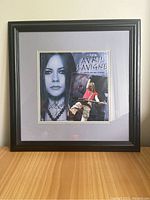 Full framed calendar cover showing black frame, light gray matting, and combined black and white and color photos of Avril Lavigne with signature.