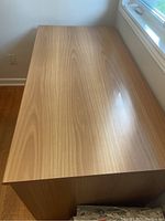 Rectangular office desk with wood finish top surface, smooth with light reflecting off it, viewed from a corner angle.