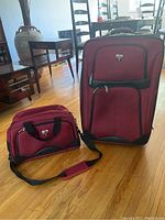 Photo showing red Swissgear suitcase and matching shoulder bag side by side on a wooden floor, both with black accents.