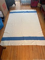 Full view of the cream wool blanket with blue horizontal stripes spread on wooden floor