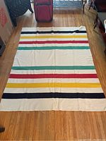 Full view of the Hudson's Bay wool blanket laid flat on a hardwood floor, showing the iconic colored stripes pattern on a cream background.