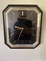 Front angled photo of the rectangular Daniel Dakota quartz wall clock with black face and gold-tone hands and hour markers, showing the brand name on the clock face.