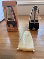 Wittner Taktell Piccolo metronome with original box and white plastic cover placed on a wooden table.