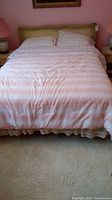 Front view of bed with pink striped comforter and pillows, showing the full width of the bed.