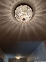 Overall view of the illuminated crystal flush mount fixture installed on a ceiling, showing light and shadow pattern down the hallway.