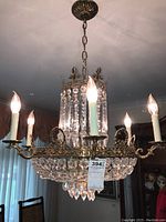 Full view of chandelier hanging from ceiling showing chain, canopy, metal frame, bulbs and crystal prisms.