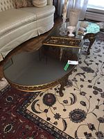 View of the coffee table showing the kidney-shaped glass top, ornate gold-toned frame, and part of the living room setting.