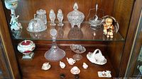 Display with multiple crystal serving pieces, miniature tea set, covered dish and porcelain figurine on right