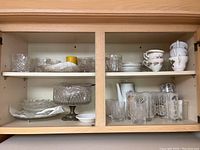Cabinet shelf top with clear glass bowls, plates, trifle dish, teacups, and saucers.