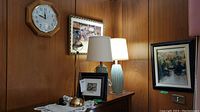 Wide view of lamps on wooden table with framed art and a clock on wall
