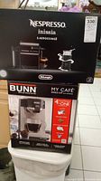Photo of boxed Nespresso Inissia with Aeroccino3 and Bunn My Cafe coffee maker stacked on top of each other.