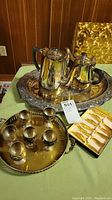 Photo showing the silver plated coffee pot and tea pot on the large oval tray, the round silver plated tray with six decorative glasses, and the box of gold plated spreaders.