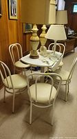 Full view of the drop leaf table with metal frame and laminate top, surrounded by four matching chairs with metal frames and vinyl seats. Several lamps and other items are placed on the table, but not included in sale.