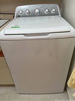 Front view of white top load washer showing closed lid and control panel on top rear side with knobs and indicators.