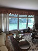 Wide view of living room window showing peach valance and white drapes with sheer curtains behind, highlighting full setup of window treatment.