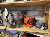 Shelf with Skyey heavy duty bench grinder, Power House grinder, grinding discs and accessories placed together.