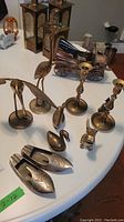 Brass decorative items displayed on white round table, including birds, candle holders, shoe-shaped pieces, and small figurines.