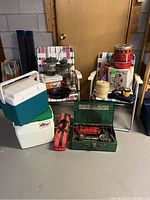 Overview of camping lot on basement floor with items grouped: coolers, chairs, lanterns, stove, heater, pan, and rope