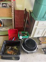 View of assorted car supplies including plastic bins, red toolbox, grease applicator bowl, and ramps stored standing upright.