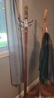 Full view of tall wood coat rack with metal hooks showing hanging jacket.