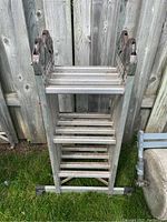 Front view of folded aluminum adjustable extension ladder leaning on a wooden fence, showing flat steps and base with non-slip feet