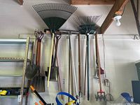 Photo of various garden tools including rakes, shovels, pitchforks, and a hand tiller hung on a wall showing condition and quantity.