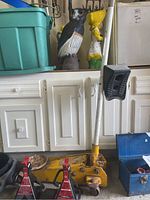 Photo of entire yellow hydraulic car jack with two red and black metal axle stands in front and green plastic tub behind.