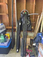 Full view of several black PVC pipes and other materials leaning against garage wall next to storage bins and tools.