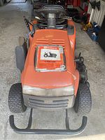 Front view of mower showing orange hood, steering wheel, seat, and owner’s manual on hood