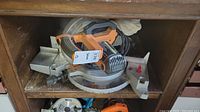 Top view of Rigid 10 inch miter saw with orange handle and gray circular saw base, showing power cord wrapped around handle and adjustable miter gauge with measurement labels.