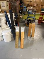 Four wooden saw horses and two blue Mastercraft metal folding saw horses standing on basement floor. White buckets are not part of the lot.