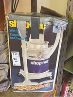 Photo of the Shop Vac in original box with tape damage at top. Shows wet/dry label and hose attachment.