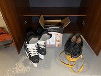 Black Hespeler Rogue ice skates size 8, black Brunswick bowling shoes with yellow carrying bag, all placed in front of wooden cabinet on concrete floor
