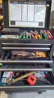 Metal toolbox open showing top tray with assorted pliers, cutters, and hand tools inside