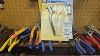Shelf with various hand tools including pliers, wrenches, and a sealed package containing metal bracelet-shaped attachments