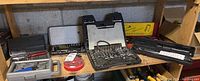 Photo of several hand tool sets arranged on a wooden shelf, showing various socket sets and screwdriver bit sets.