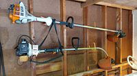 Two Stihl gas trimmers (FS55R and FS52) hanging on a garage wall