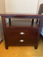 Front view of the wooden bedside table showing two drawers with silver handles and an open shelf above.