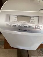 Top control panel of Panasonic SD-RD250 automatic bread maker showing digital display and buttons for selection including size, crust darkness, timer, start/stop.