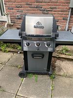 Front view of Broil King Monarch gas BBQ grill showing control panel with three knobs, side shelves, wheels, and overall structure.