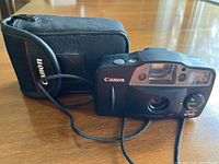 Canon Sure Shot Owl 35mm camera alongside the black Canon-branded carrying case on wooden surface.
