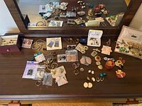 Photo showing a variety of earrings, brooches, and pendants laid out on dresser top with reflections in mirror.